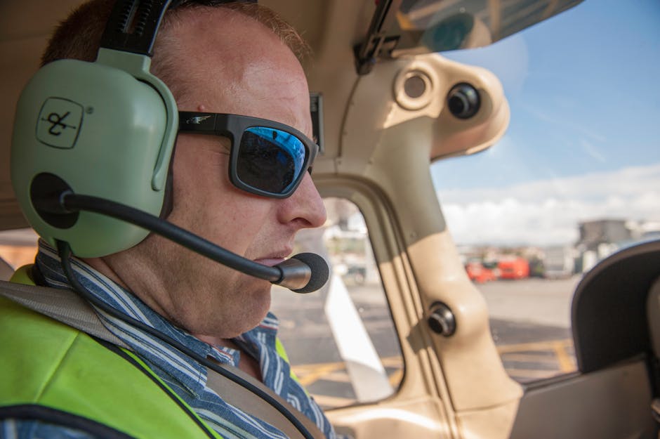 A pilot wearing sunglasses and a headset in the cockpit during a clear day.